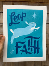 Load image into Gallery viewer, A print with the text, &quot;Leap of Faith&quot; with a bunny leaping across a teal background under an 8-pointed star.
